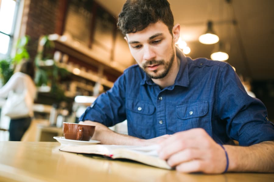 man reads bible while drinking coffee