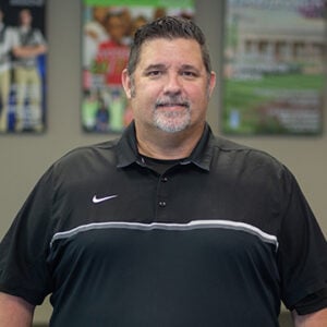 A man with short spiked black hair and a salt and pepper goatee is wearing a black Nike shirt and smiling at the camera.
