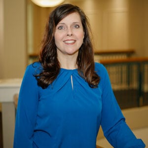 A woman with brunette hair wearing royal blue shirt and smiling.