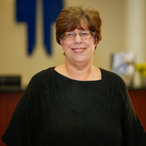 A woman with short brunette hair is wearing glasses and a black top while smiling.