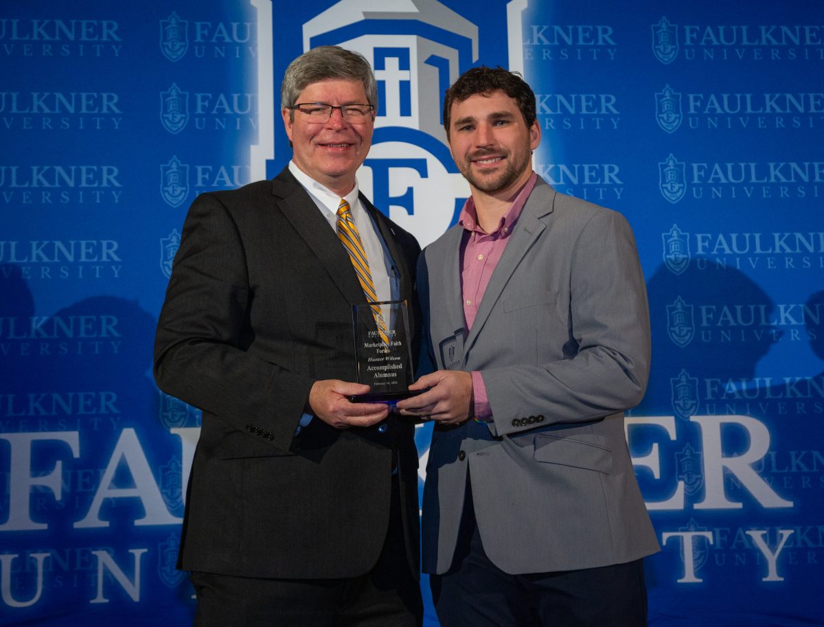 President Mitch Henry presents Hunter Wilson with the Accomplished Alumnus Award in front of a Faulkner blue backdrop. 