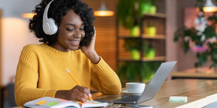 Student wearing yellow sweater smiling while studying on laptop