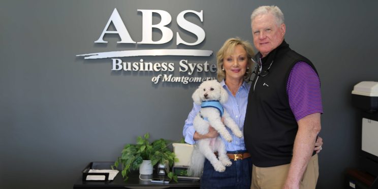 l-r Judy and Eddie Cobb stand in front of the ABS logo. They are supporters of the Zorn Scholarship Fund.