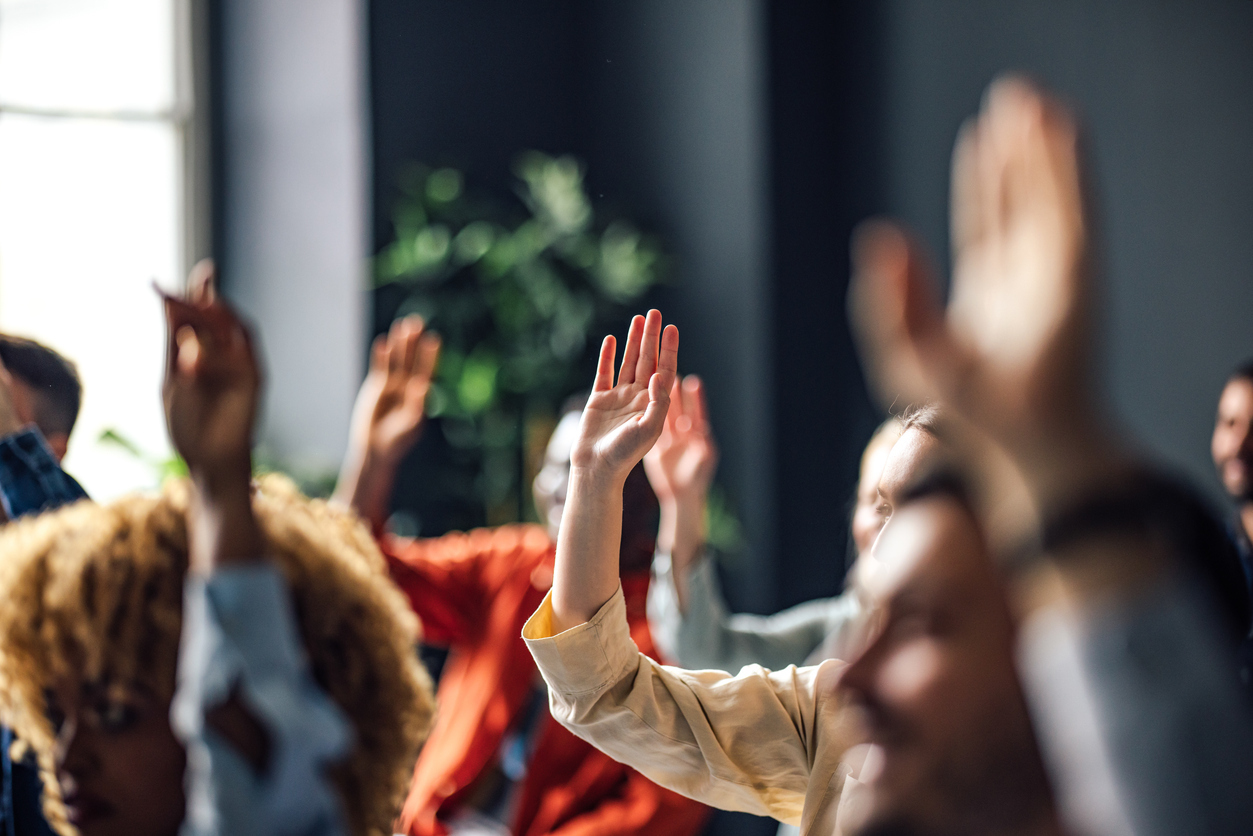 Group of adult students raising hands at seminar